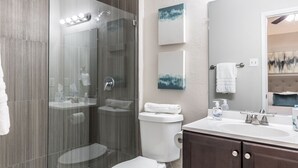 A modern bathroom with a glass-enclosed shower, a white toilet, a vanity with a sink, and a large mirror.