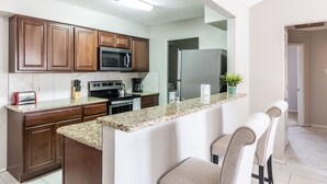A modern kitchen with wooden cabinets, granite countertops, a microwave, stove, and a refrigerator.