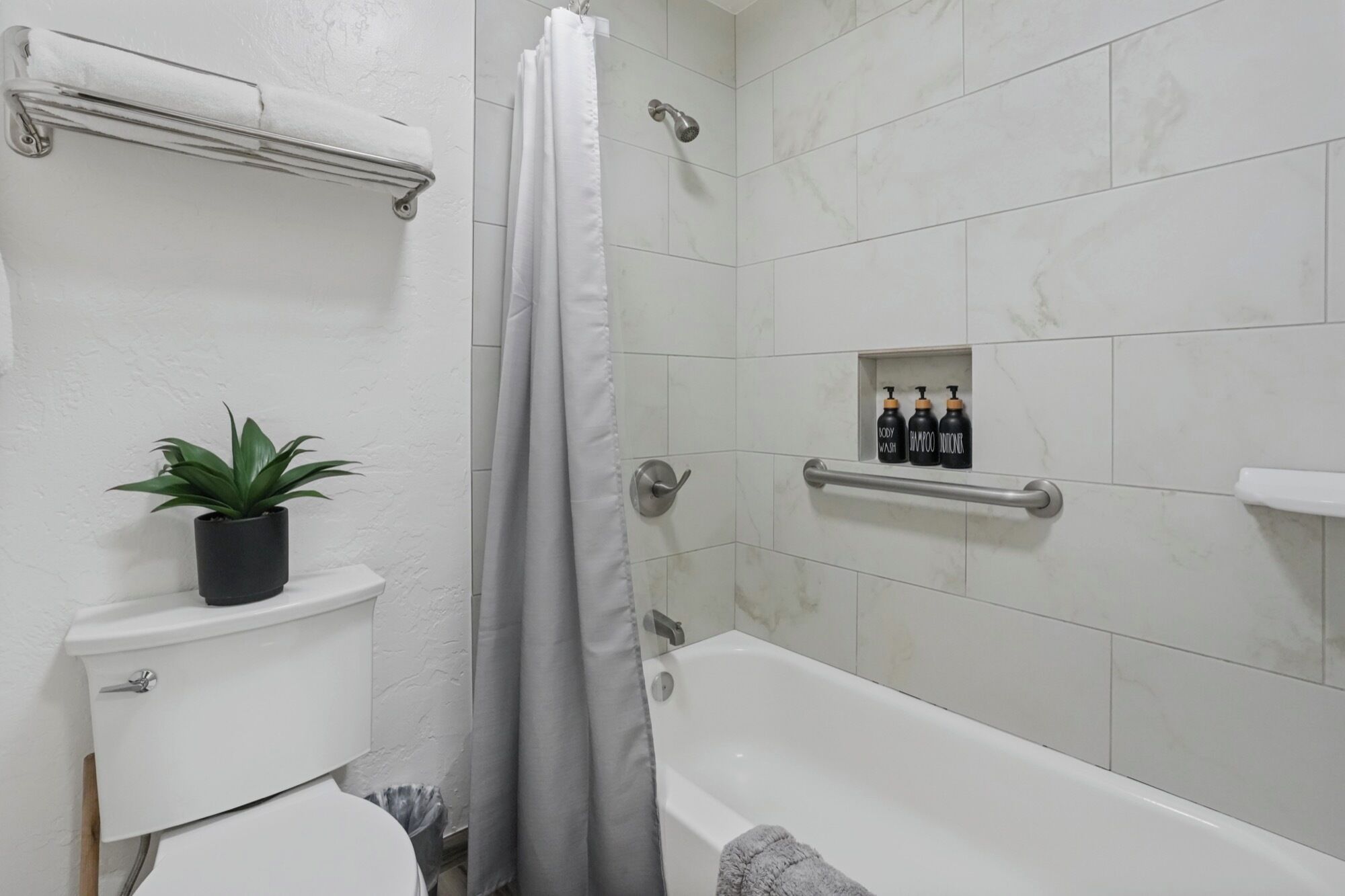 Un baño con inodoro, ducha con cortina, bañera, estante con artículos de aseo e instalación de plantas.