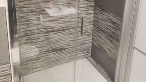 A glass-enclosed shower with a modern design, featuring a textured wall and a visible drain. - Soffio di Relax (Palermo)