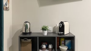 A modern living space with a mounted TV, a coffee maker, a kettle, a plant, and a shelf with various items including a bag and a box. - Soffio di Relax (Palermo)