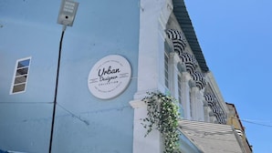 A building with a blue facade, a circular sign reading "Urban Designer Collection," and a window with a view of the sky. - Urban Designer Collection Lebuh Melaka (George Town)