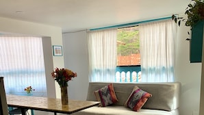 A living room with a sofa, a dining table, and a window with curtains. - Cozy apartament in the most popular and colorful artesans street in Pisac (Písac)