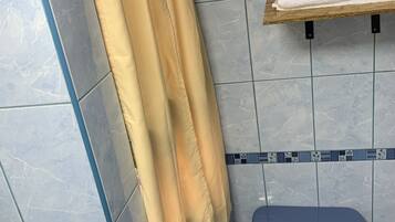 A bathroom with a blue toilet, a towel rack with a folded towel, and a shower curtain.