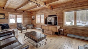 A log cabin interior with a wooden ceiling, a large TV, a sofa, and a coffee table.