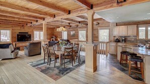A spacious living area with a large wooden ceiling, a dining table surrounded by chairs, a sofa, and a television.