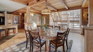 A spacious dining area with a wooden table and chairs, a chandelier, and a view of the outdoors through large windows.