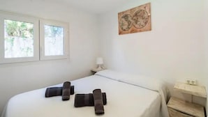 Habitación de hotel con cama, mesita de noche con lámpara, obra de arte en la pared y ventana con vista a follaje.