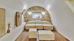 A cozy, semi-open living space with a stone arch, a cushioned seating area, and wooden flooring.