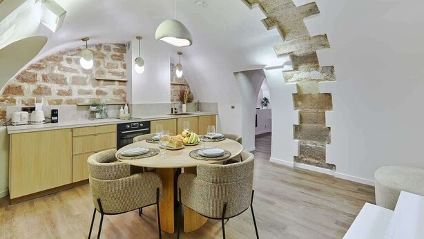 A modern kitchen with a stone wall, wooden ceiling, and a dining area with wicker chairs and a round table.