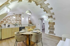 Una cocina moderna con pared de piedra, techo de madera y una zona de comedor con sillas de mimbre y una mesa redonda.