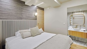 A modern hotel room with a large bed, a wooden headboard, a marble bathroom vanity, and a large mirror.