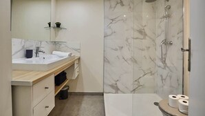 Ein modernes Badezimmer mit einer gläsernen Duschkabine, einer Wand mit Marmorfliesen, einem Waschbecken mit Spiegel und einer Toilette.