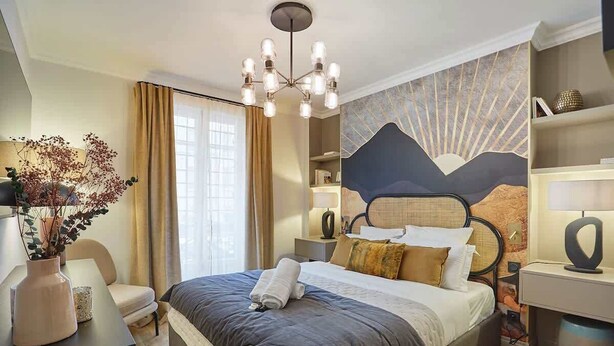 A modern hotel room with a large bed, a chandelier, a desk with a vase, and a wall mural. - Superb new flat Notre Dame de Paris (Paris)