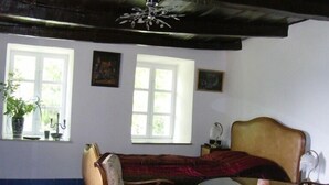 Una habitación con un tapete estampado, un banco de madera, una mesa redonda y dos sillas. Hay ventanas con cortinas, un ventilador de techo y una planta en maceta.