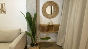 A room with a beige sofa, a potted plant, a round mirror, and a wooden shelf with a white vase. - A (VA070.2.9) TH Mediterranean Suites 9 (Valencia / València)