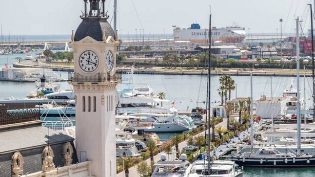 A marina with boats docked, a clock tower, and a large ship in the background. - A (VA070.2.9) TH Mediterranean Suites 9 (Valencia / València)