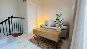 A modern living room with a wooden coffee table, a grey sofa, a white vase with a plant, and a staircase with black railings.