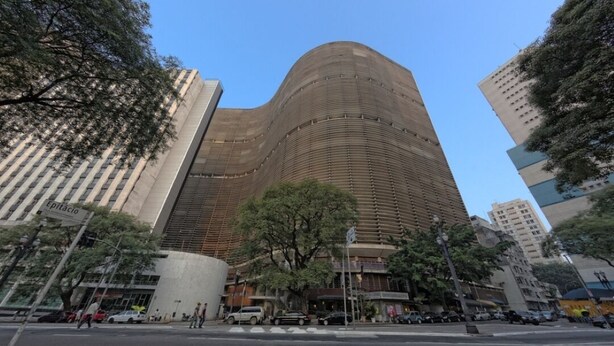 Un edificio moderno con fachada curva, rodeado de árboles y otras construcciones urbanas.