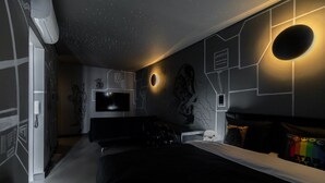Un dormitorio moderno con techo estrellado, una cama grande, un televisor y almohadas con temática de Star Wars.