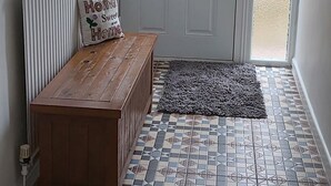 Ein Zimmer mit einer hölzernen Sitzbank, einem Heizkörper, einer Tür mit satinierten Glasscheiben und einem gemusterten Boden.