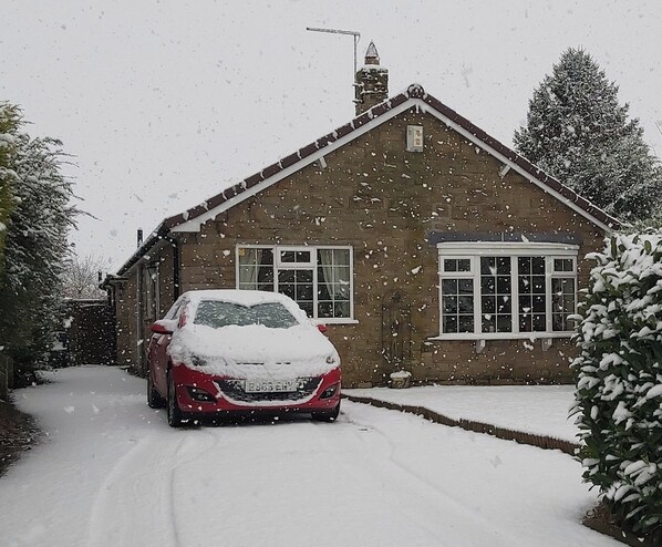 Una calle residencial nevada con una casa y un coche cubiertos de nieve.