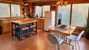 Cocina de cabaña de madera con una isla central, armarios de madera y un ventanal con vistas a un bosque.