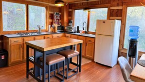 Cocina de cabaña de madera con una isla central, armarios de madera, un refrigerador blanco y un dispensador de agua.