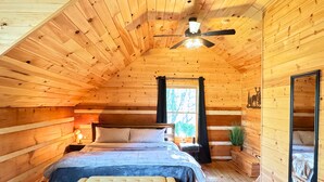 Acogedor dormitorio tipo cabaña de madera con cama, mesita de noche y ventilador de techo.