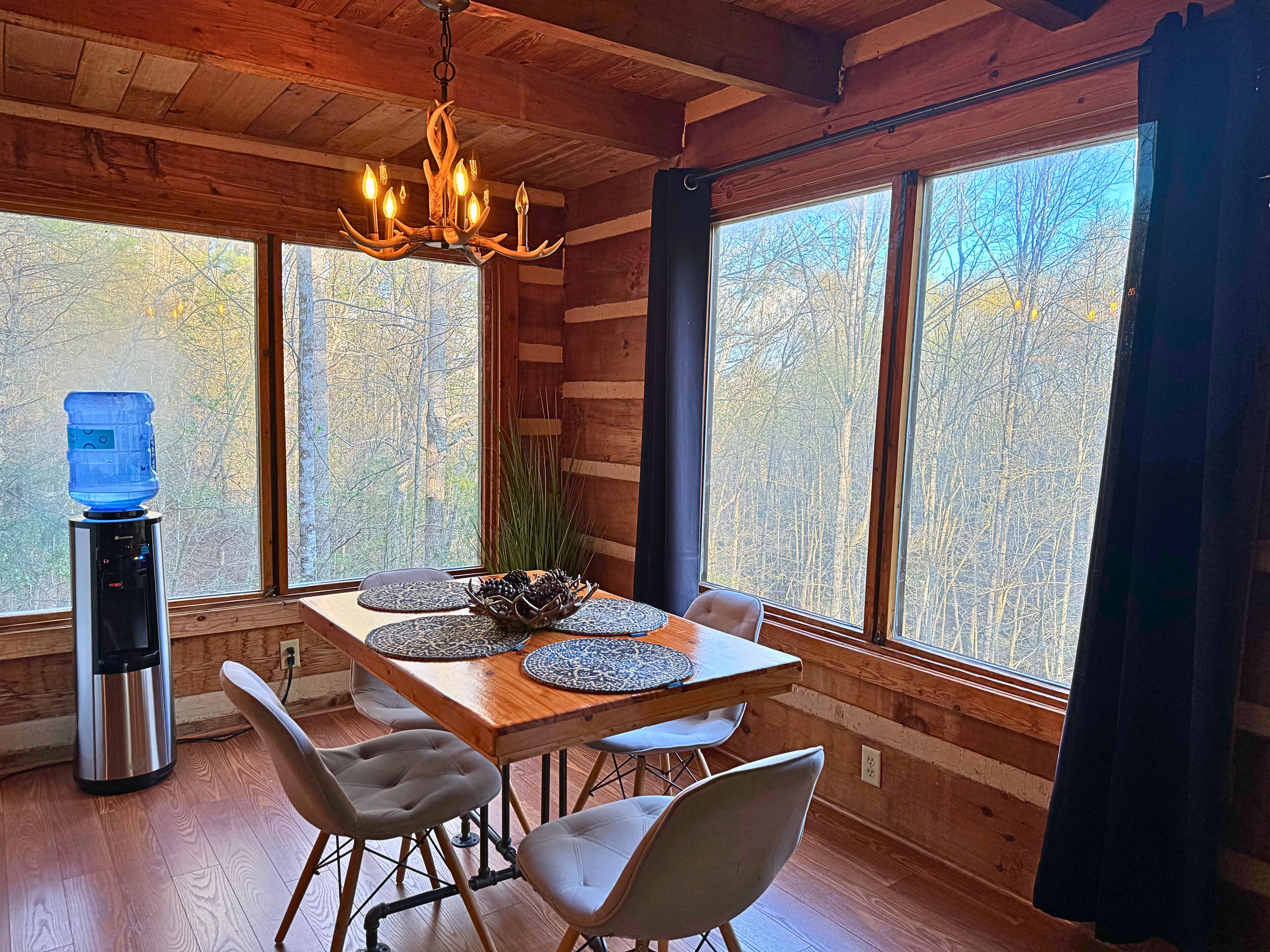 Un coin repas aménagé dans une cabane en bois, avec une table pour quatre personnes, un distributeur d’eau et un lustre.
