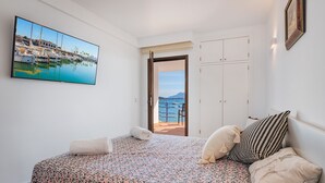 Ein Schlafzimmer mit Bett, Kissen, einem Gemälde und Meerblick durch eine offene Tür.