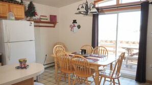 Une cuisine équipée d’un réfrigérateur, de meubles de rangement en bois, d’une table à manger avec des chaises, et offrant une vue sur un patio extérieur.