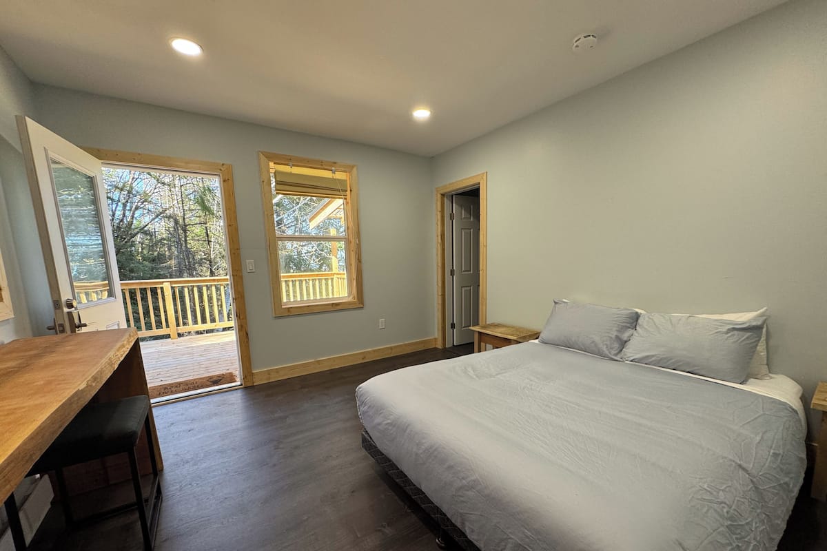 A bedroom with a large bed, a wooden desk, and a balcony with a wooden railing.
