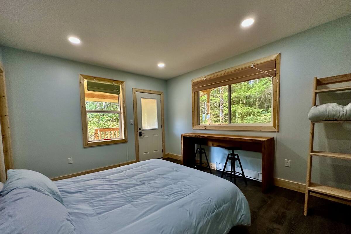 A bedroom with a bed, a desk, and two windows.