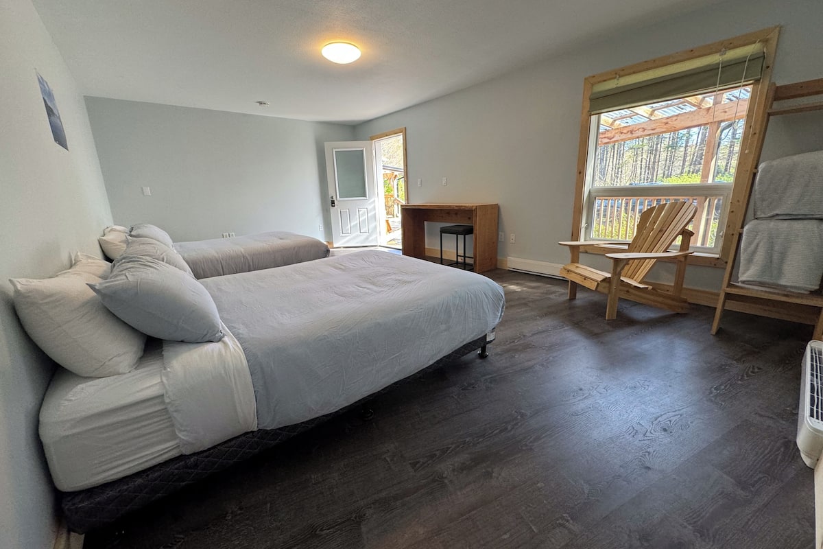 A bedroom with a large bed, a wooden desk, a chair, and a window with a view of trees.