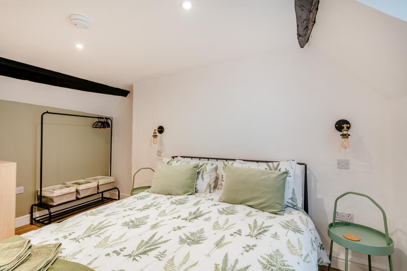 A bedroom with a bed, a mirror, a wall-mounted light fixture, and a green chair.