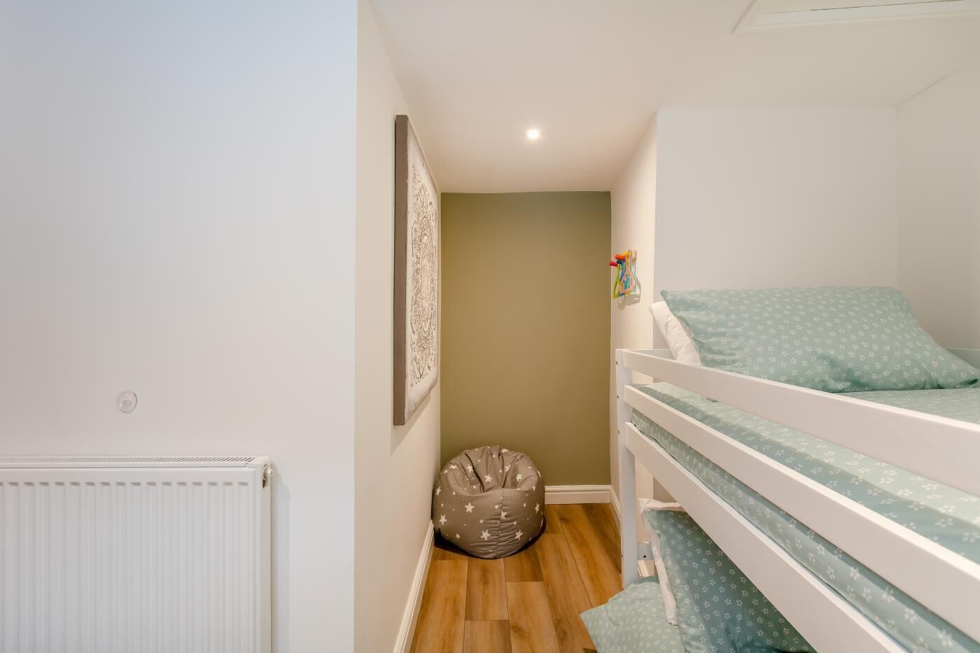 Una habitación infantil con una cama litera, un sillón de peluche, un radiador y un cuadro en la pared.