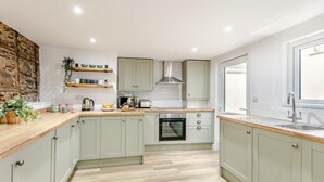 Une cuisine moderne avec des meubles de couleur vert clair, un plan de travail en bois, un four encastré et une fenêtre qui laisse entrer la lumière naturelle.