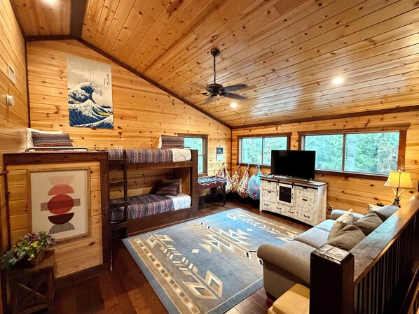 A wooden cabin interior with bunk beds, a television, a sofa, and a ceiling fan.