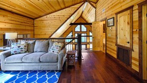 Een knus interieur van een chalet met een bank, houten wanden, een trap en een groot raam.