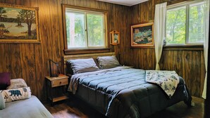 Een slaapkamer met een houten wand, een bed met quilt, een nachtkastje en twee ingelijste foto's.