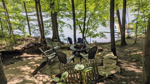 Een terras aan het meer met Adirondack stoelen en een vuurkorf.