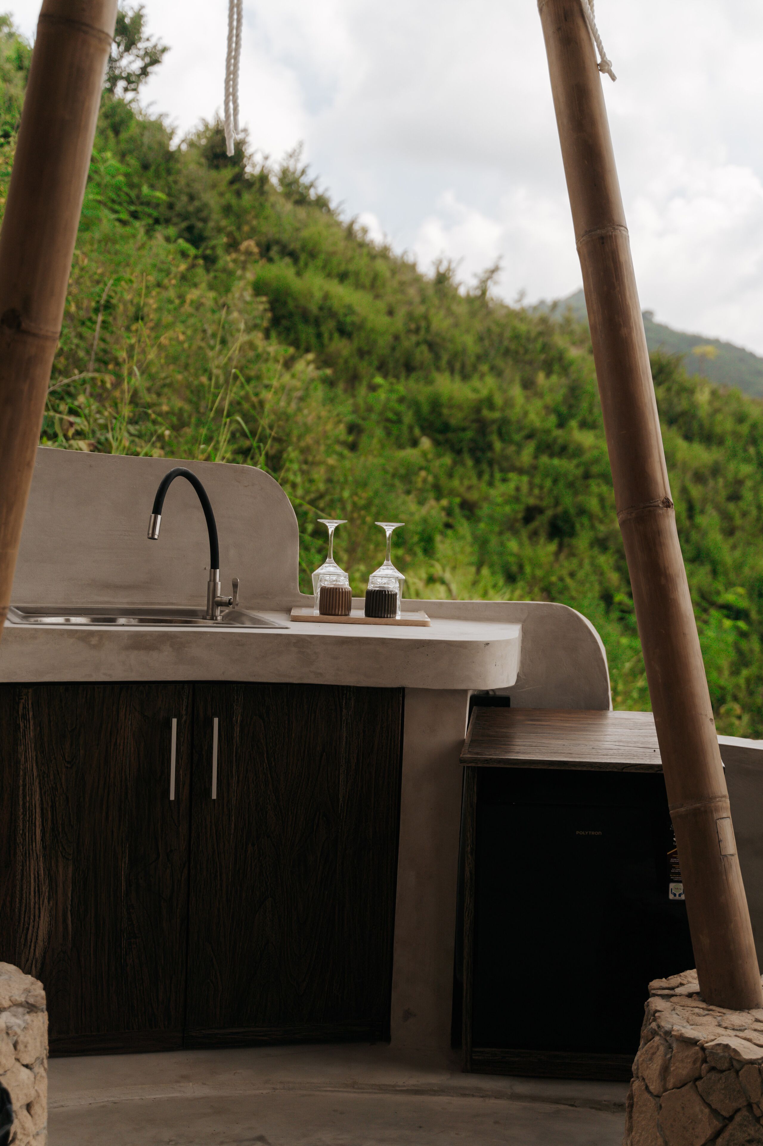 Cocina exterior con un lavamanos, dos copas de vino y un refrigerador pequeño.