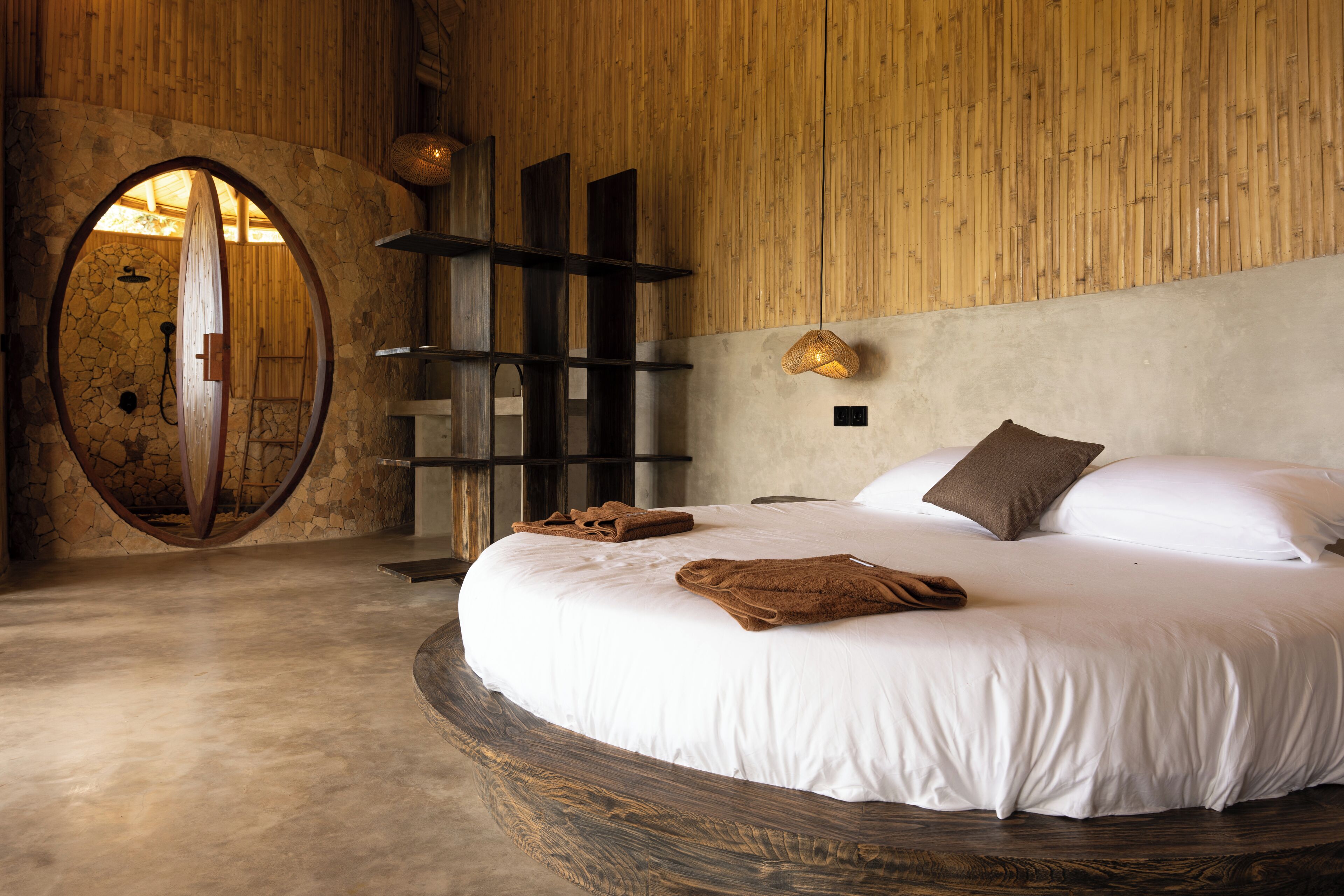 A circular bed with white linens, a stone arch doorway, and a wooden wall.
