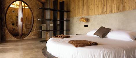 A circular bed with white linens, a stone arch doorway, and a wooden wall.