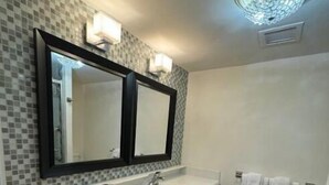 Une salle de bain avec deux lavabos, un grand miroir et une douche. Des serviettes sont suspendues sur un porte-serviettes et il y a un tapis sur le sol.