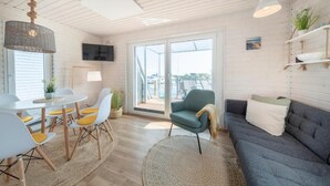 A modern living room with a dining area, a grey sofa, a blue armchair, and a TV mounted on the wall. - Hausboot Rán für 5 Pers. mit Großzügiger Dachterrasse in Kragenæs auf Lolland (Schleswig)