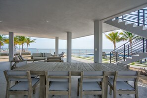 A wooden deck with a table and chairs, overlooking a beach with palm trees and a staircase leading to an upper level. - Oceanfront Luxury Mansion, Dock, Pool&Spa, Kayaks (Marathon)