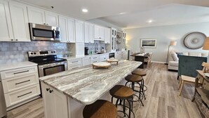 A modern kitchen with white cabinets, a marble countertop, and a central island with stools.