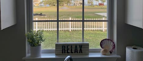 A kitchen with a window, a sink, a potted plant, a 'RELAX' sign, and a view of a fenced yard.